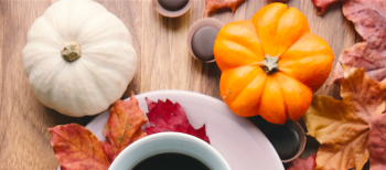 Orange and white pumpkins next to a coffee cup with autumn leaves