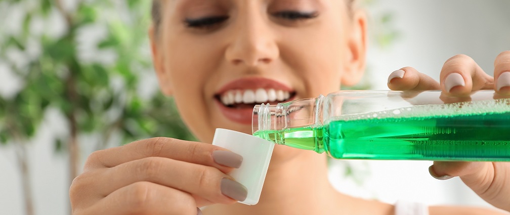 A woman pouring green mouthwash as part of her oral hygiene routine